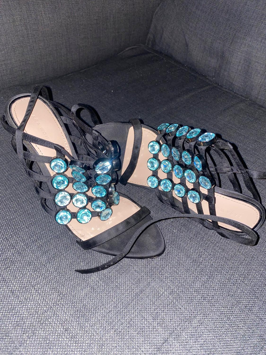 Close-up of black sandals with blue rhinestones on criss-cross straps.