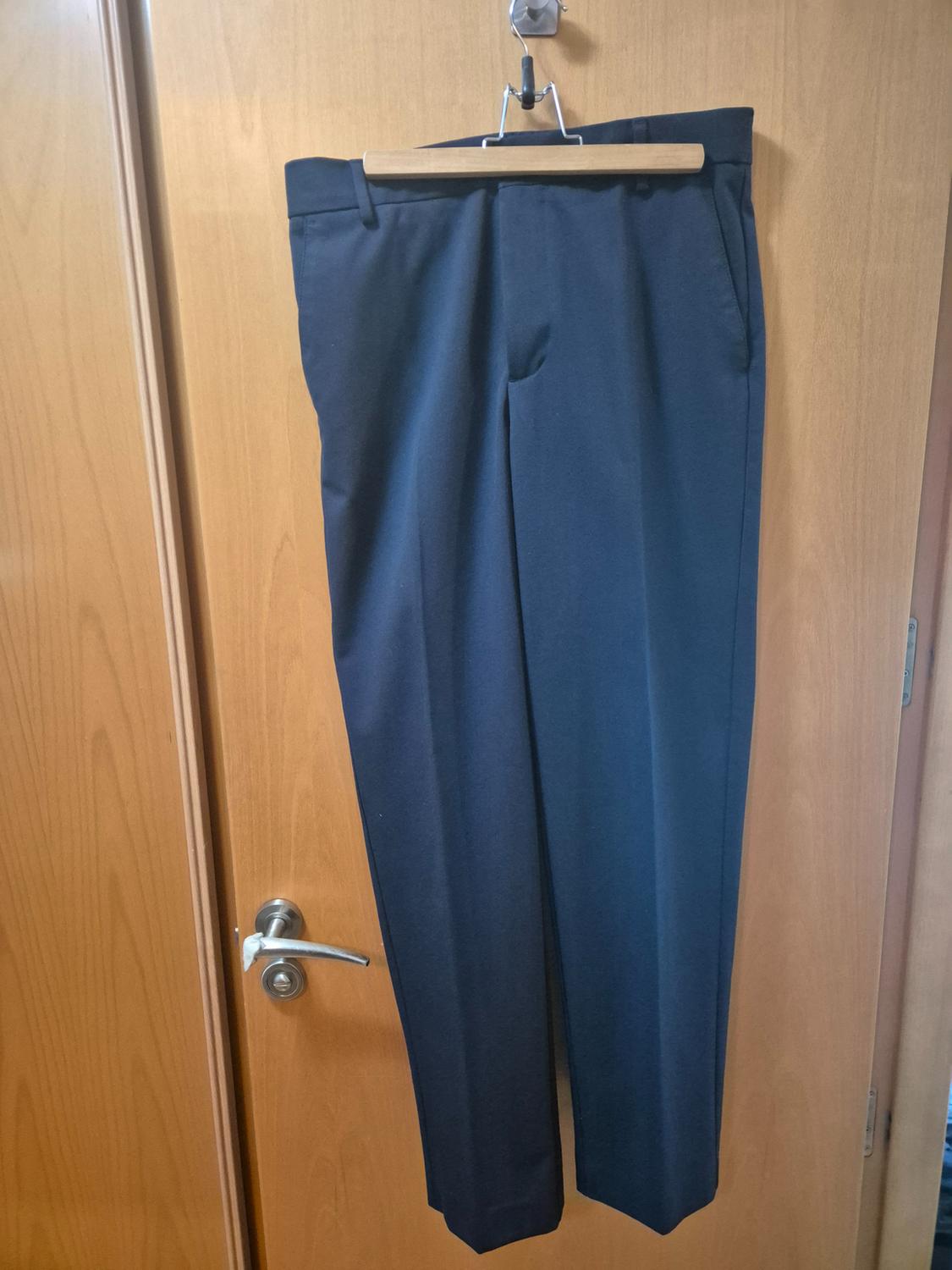Dark blue trousers hung on a wooden hanger over a light wooden door with a silver handle.