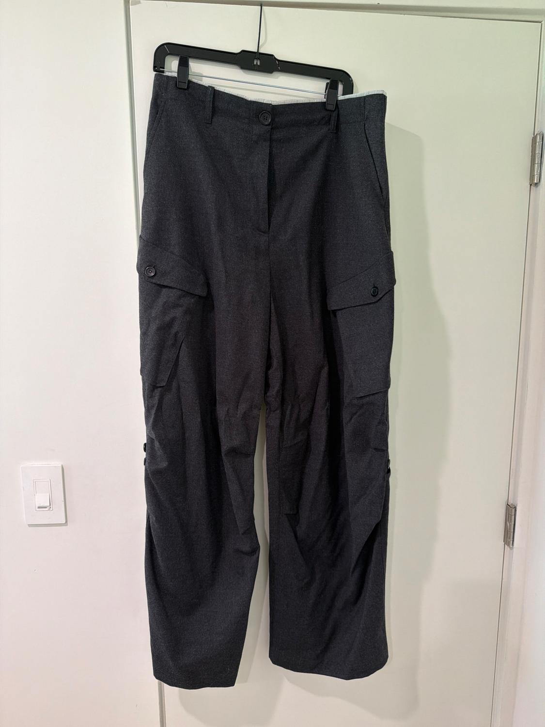 Dark grey wide-leg cargo trousers with side pockets, hanging on a black hanger on a white door.