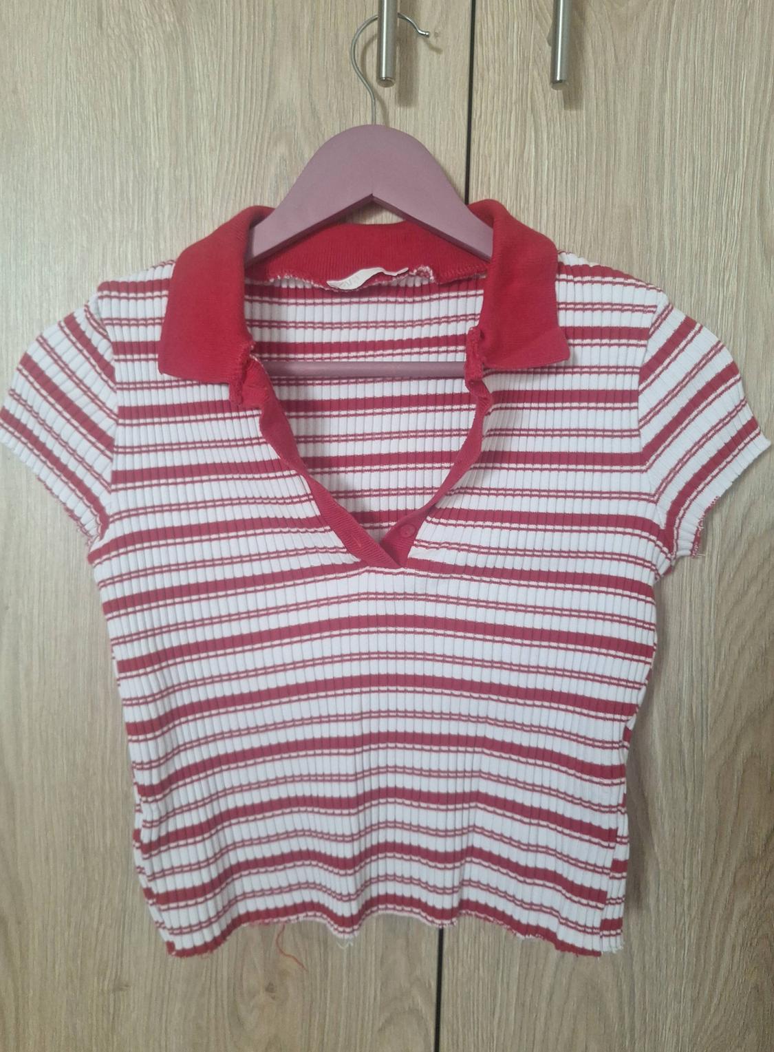 Red and white striped short-sleeved t-shirt with a red polo collar, hanging on a pink hanger in front of a wooden wardrobe.