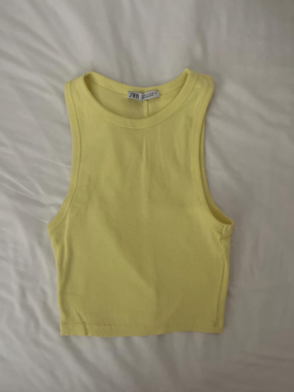 Light yellow sleeveless ribbed crop top with ZARA label, on a relaxed-style crumpled white sheet.