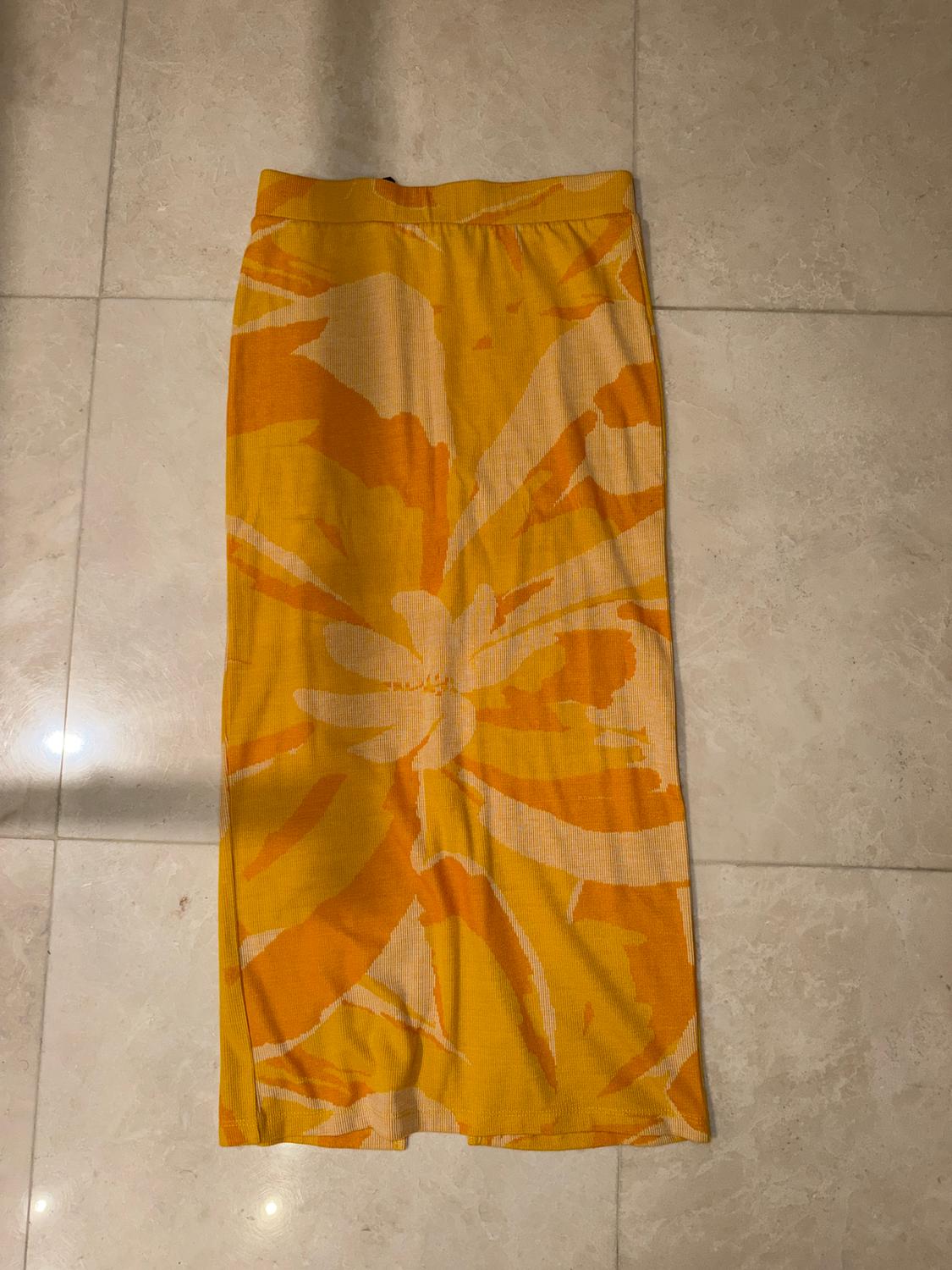 Long yellow skirt with a floral pattern in orange and beige tones, on a light tiled floor.