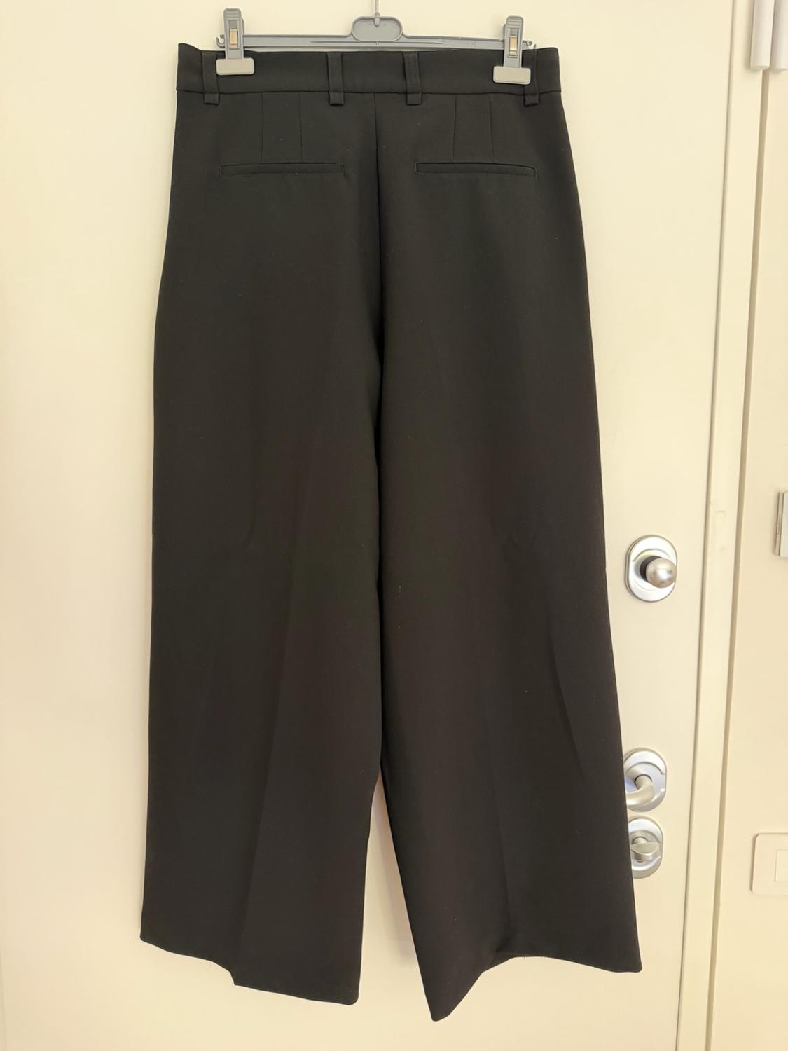 Black wide-leg trousers hanging on a coat hanger over a light-coloured door. Rear view with belt loops and pockets.
