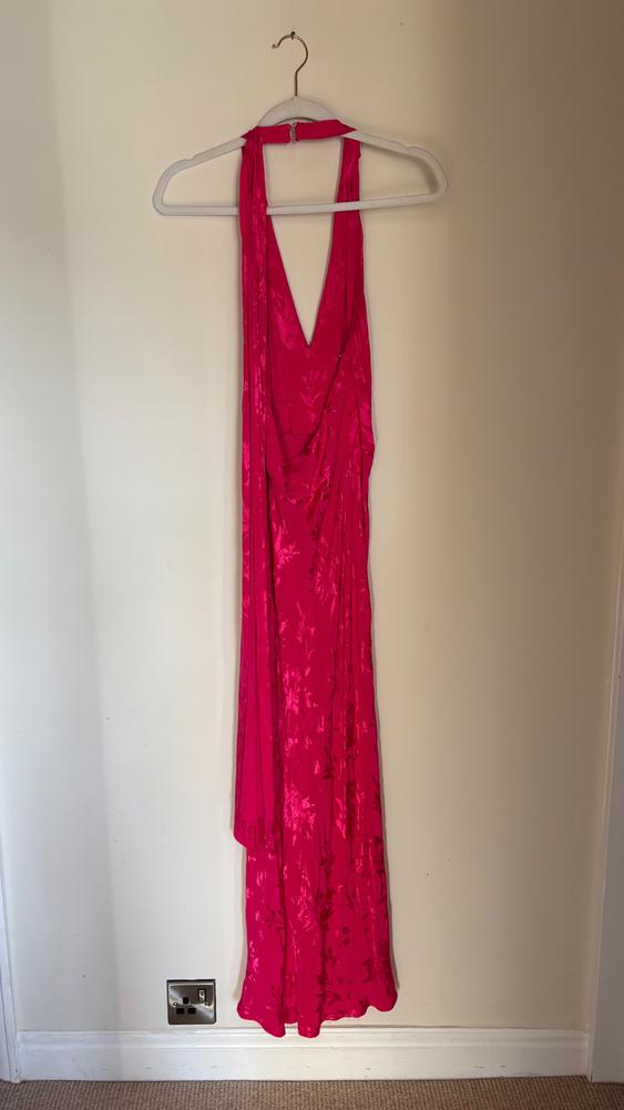 Bright pink long dress with a floral print hanging on a white hanger against a light wall.