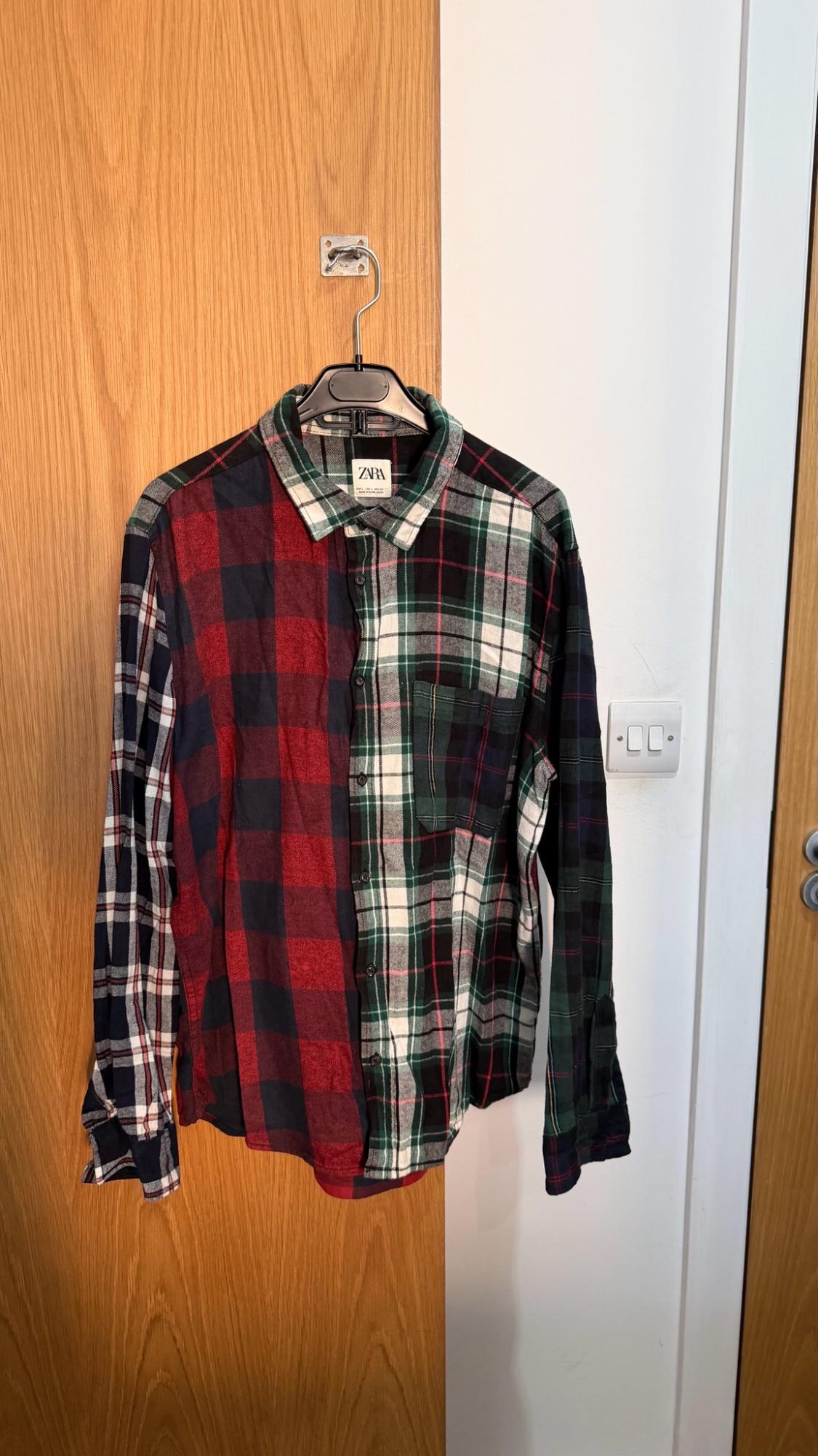 Mixed check shirt in shades of red, green and navy blue hanging on a wooden door next to a white wall. ZARA label.