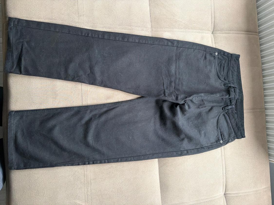 Black straight-leg jeans laid out on a beige upholstered sofa.