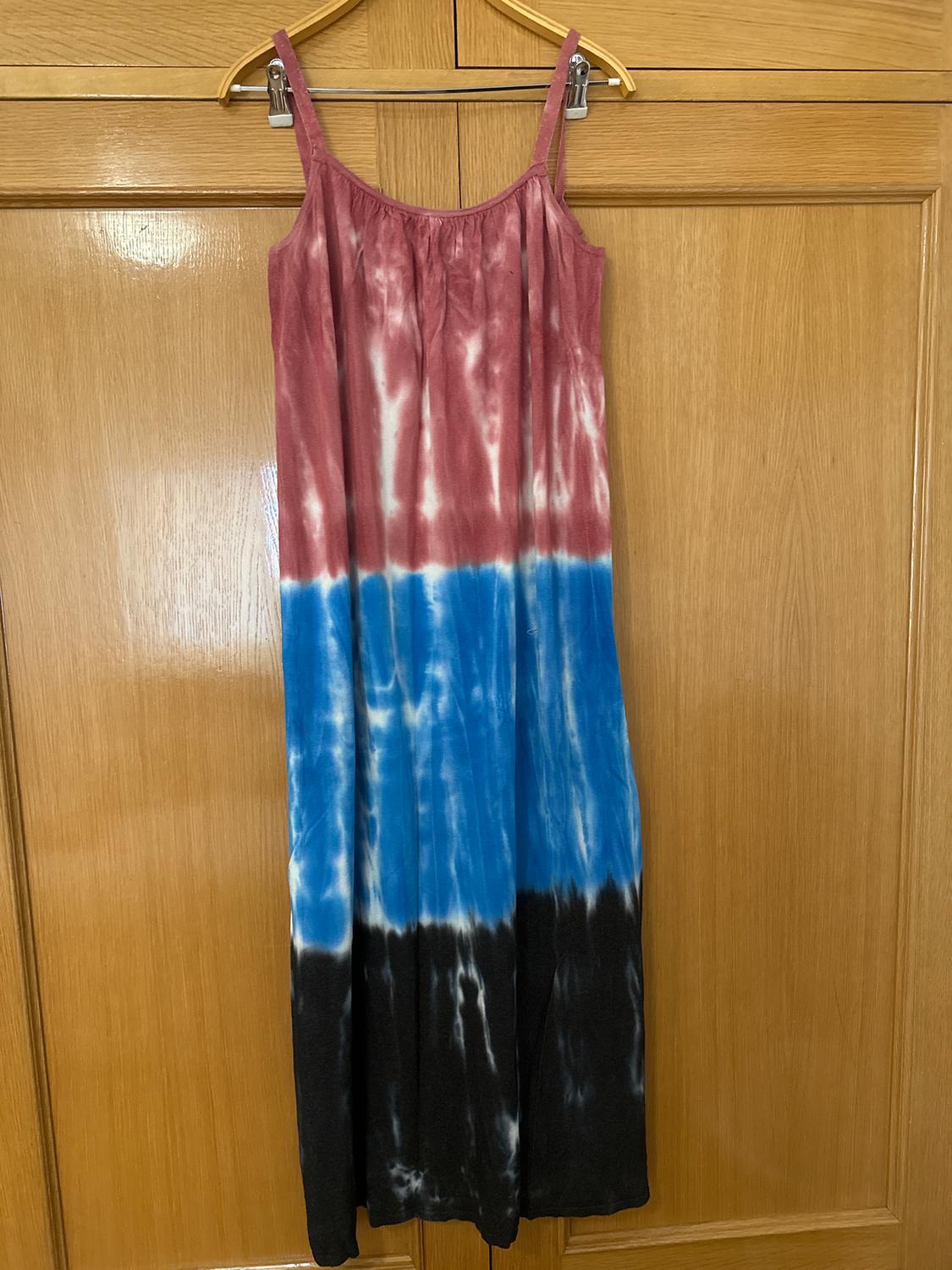 Long, strappy dress with a tie-dye design in shades of red, blue, and black, hanging on a wooden hanger in front of a wardrobe door.