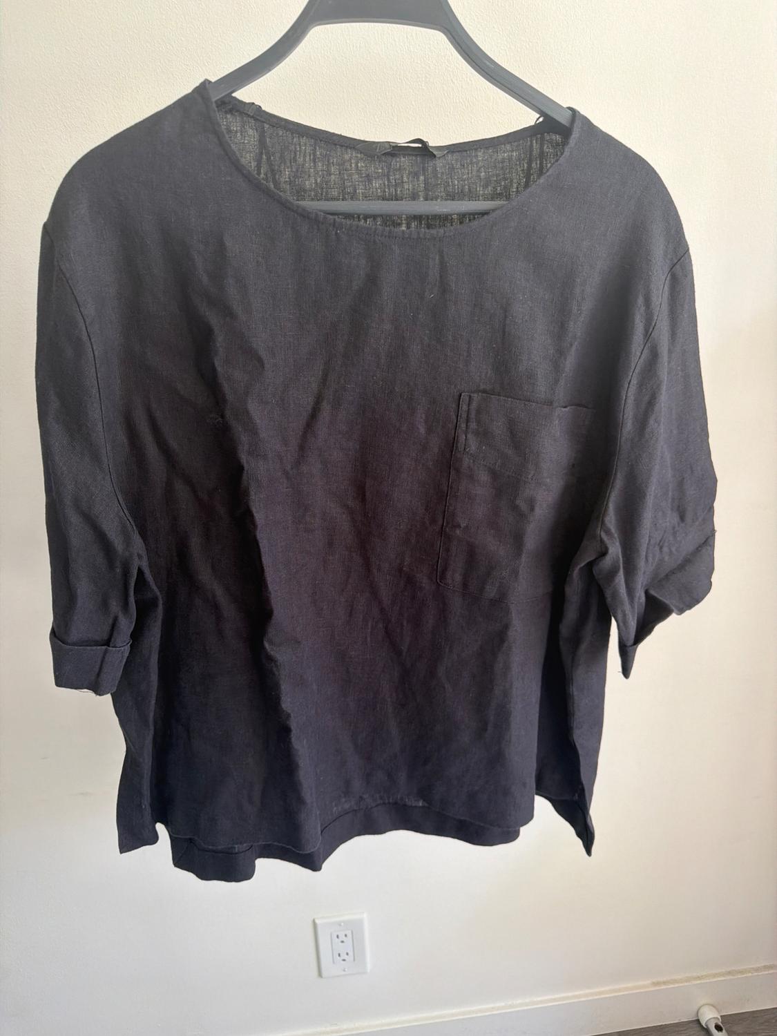 Black short-sleeved T-shirt with a chest pocket, hanging on a black hanger against a white background.