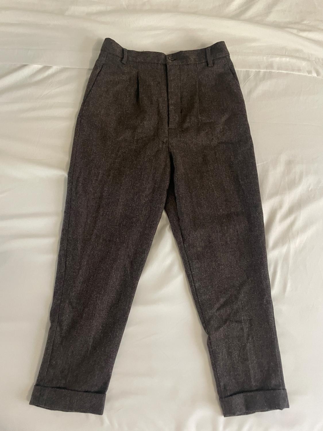 Dark brown tailored trousers with pleats and turn-ups, laid out on a white sheet.