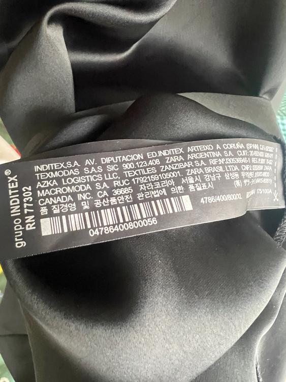 Black label with white Inditex text on dark fabric. Includes addresses, barcodes, and reference numbers.