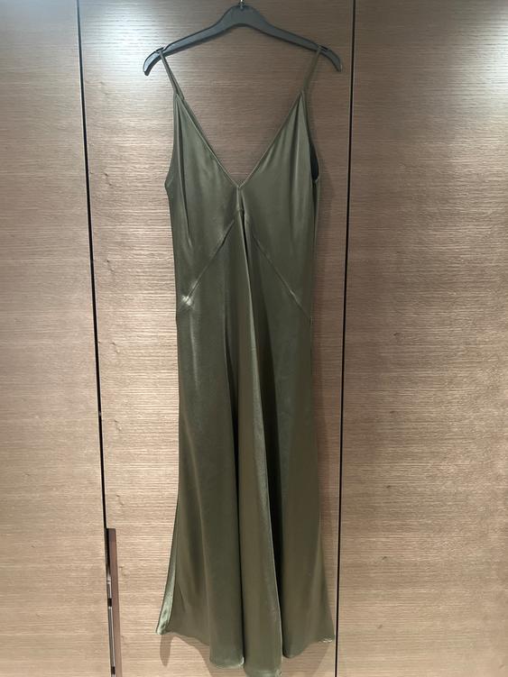 Olive green spaghetti strap dress hanging on a hanger over a light wooden door.
