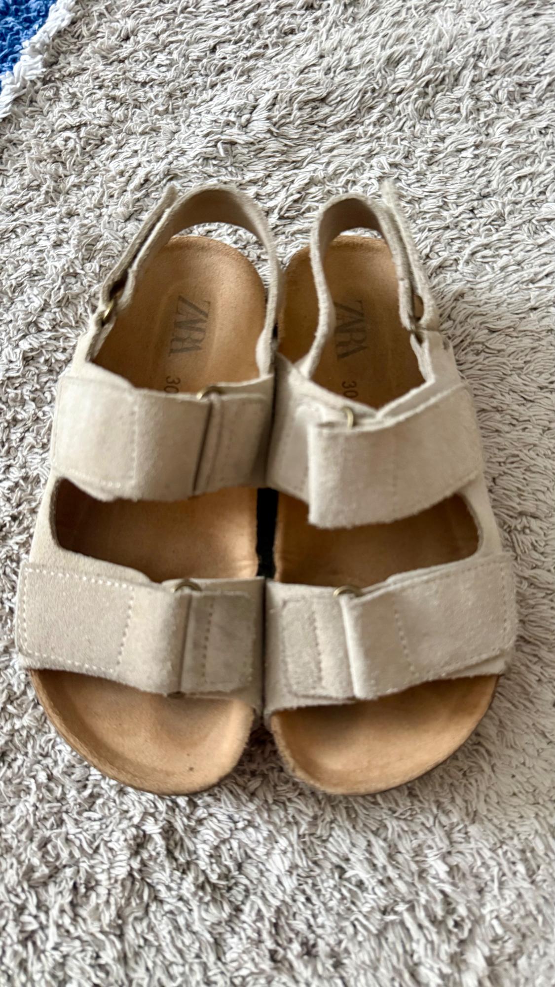 Beige sandals with adjustable straps resting on a textured rug. The insole reads ZARA 30.