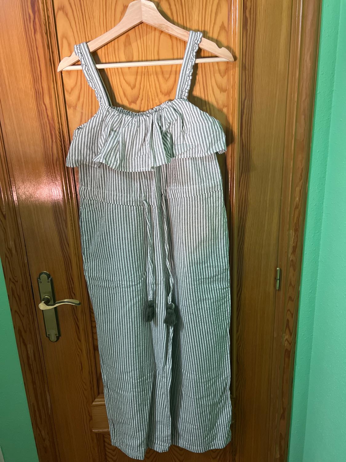 White and grey striped romper hanging on a wooden hanger over a wooden door. It has straps and ruffles on the chest.