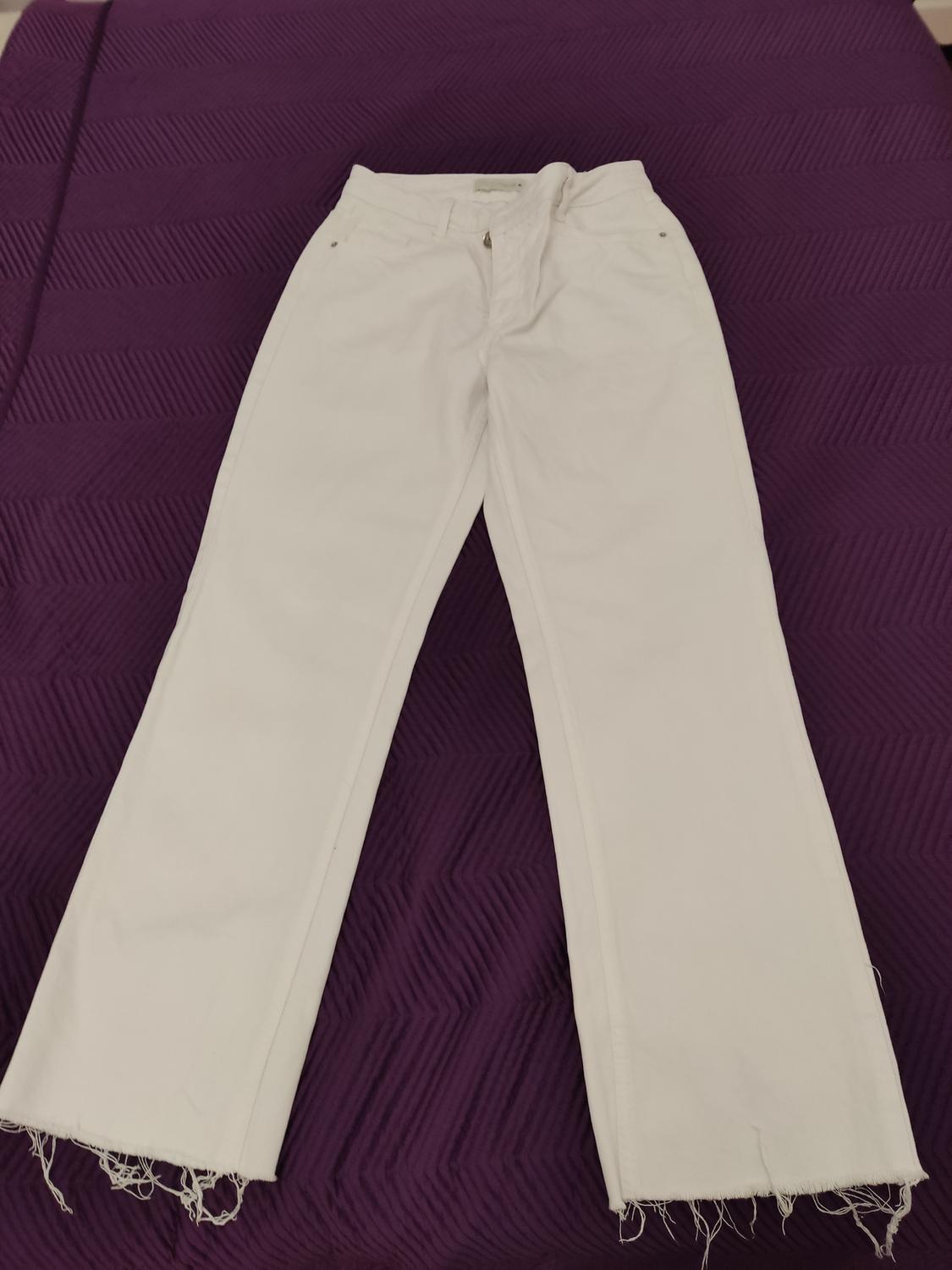 White denim jeans with a frayed hem, placed on a purple geometric patterned quilt.