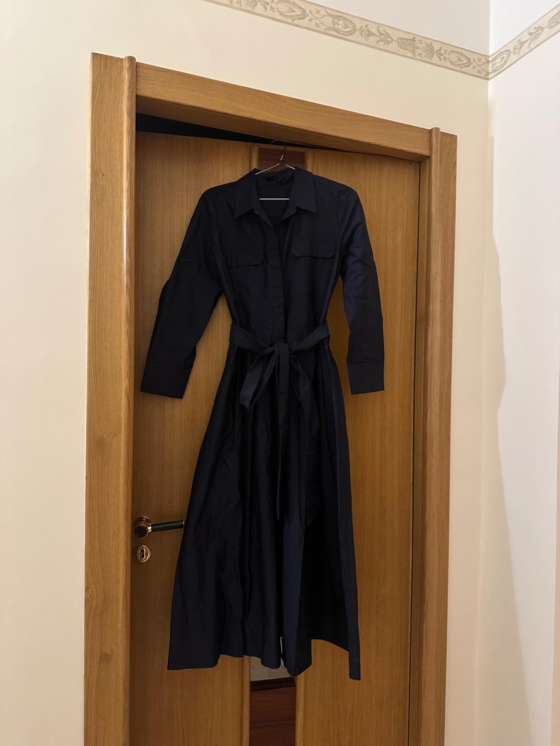 Navy blue maxi shirt dress with pockets and belt, hanging on a wooden door in a relaxed and casual interior setting.