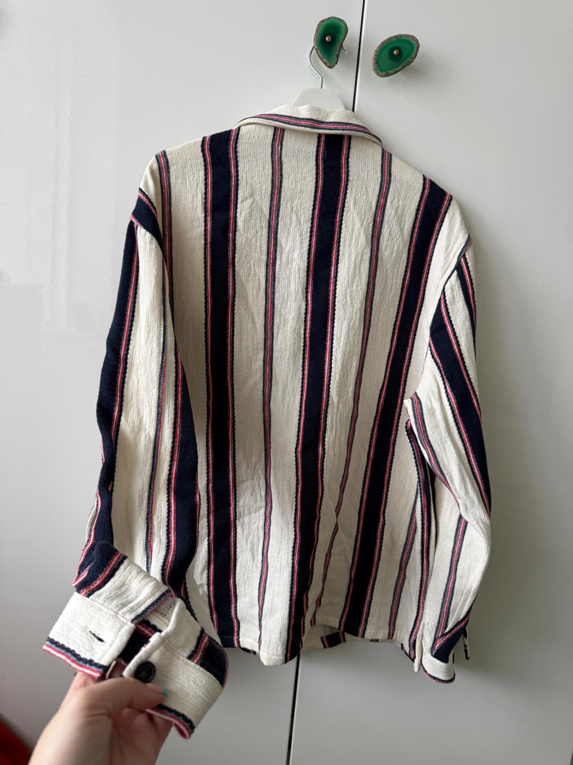 A shirt with vertical white, blue and red stripes is hanging on a hanger. A hand is holding the end of the sleeve.