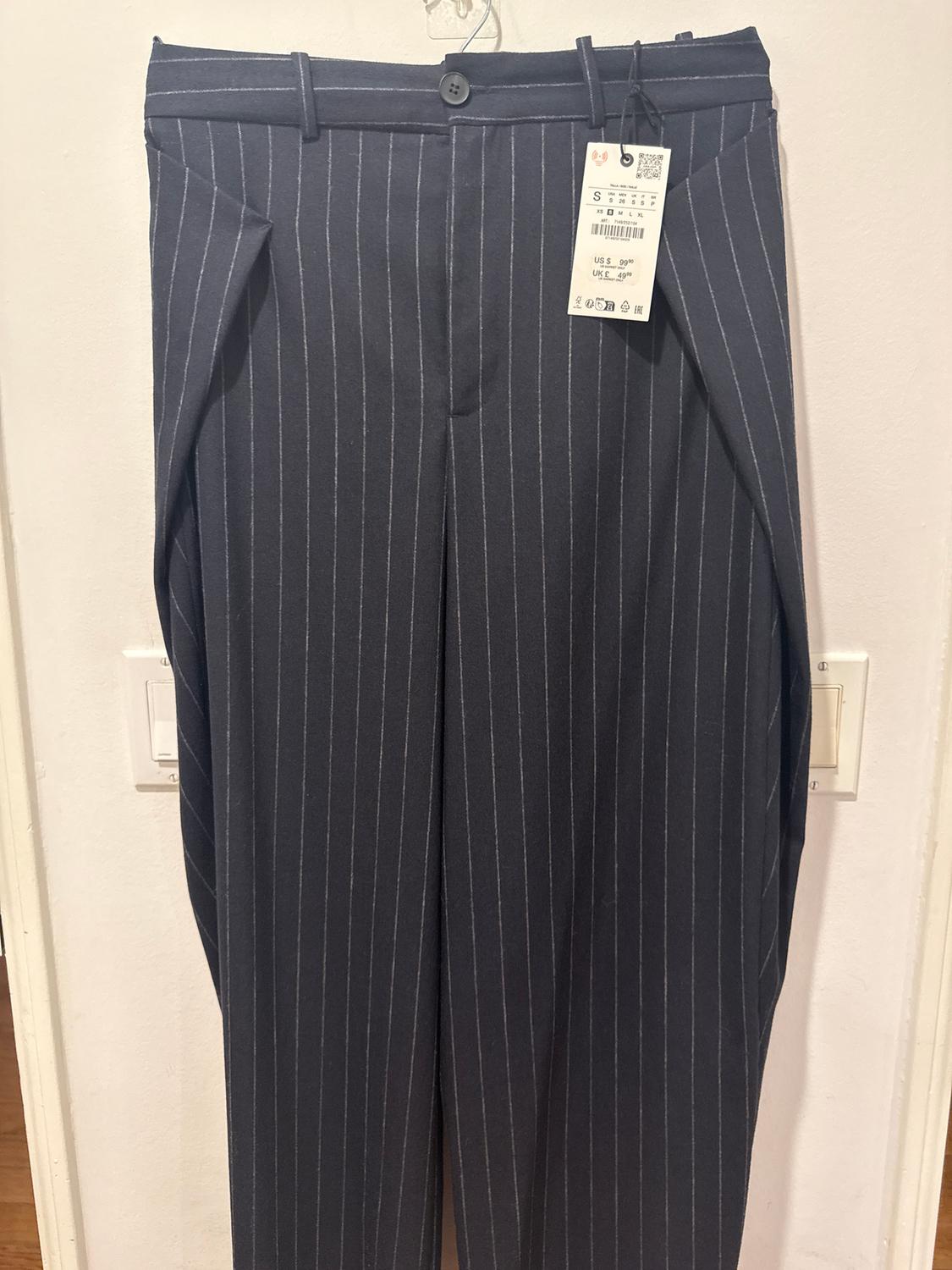 Navy dress trousers with white vertical stripes, hanging on a hanger. Visible tag with size and price details.