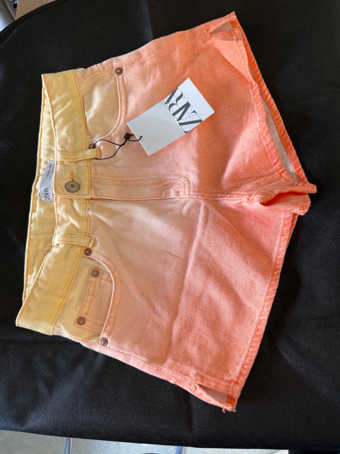 Front view of gradient shorts in orange and yellow with front pockets and visible tag.