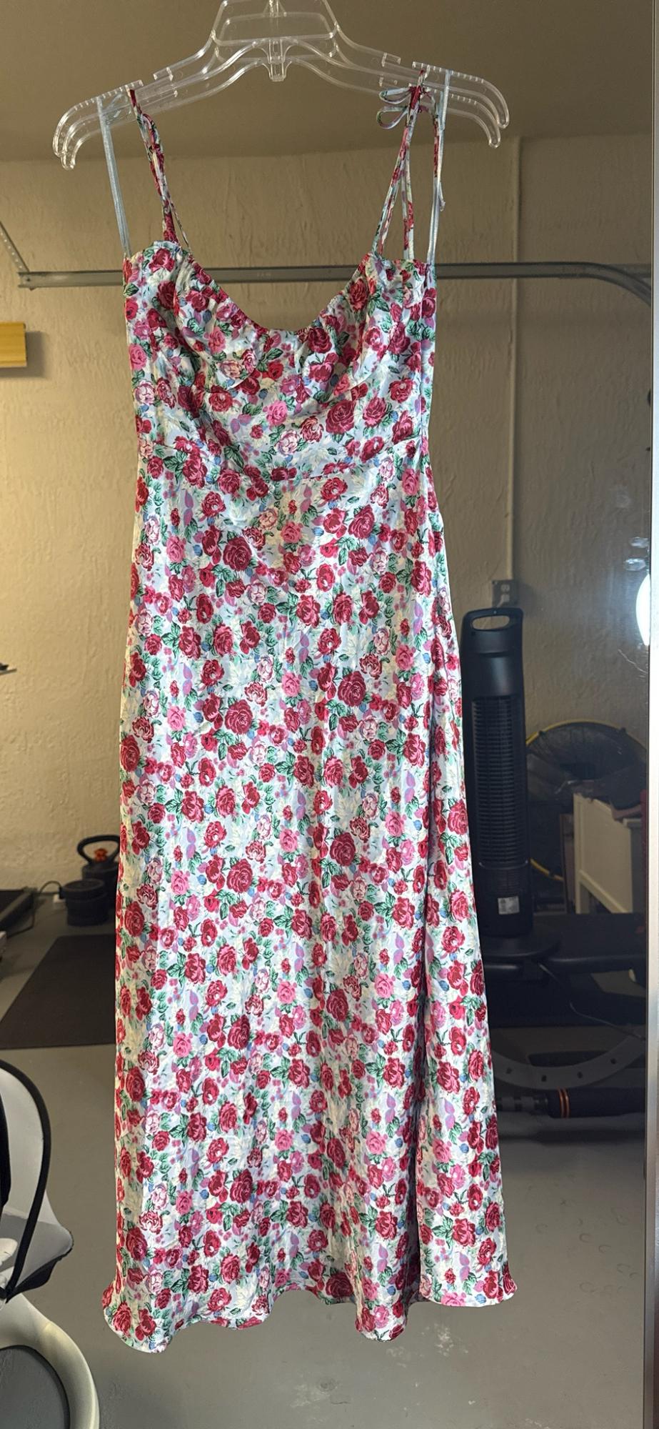 Red and pink floral print maxi dress with straps, hanging on a clear hanger in a garage with beige walls.