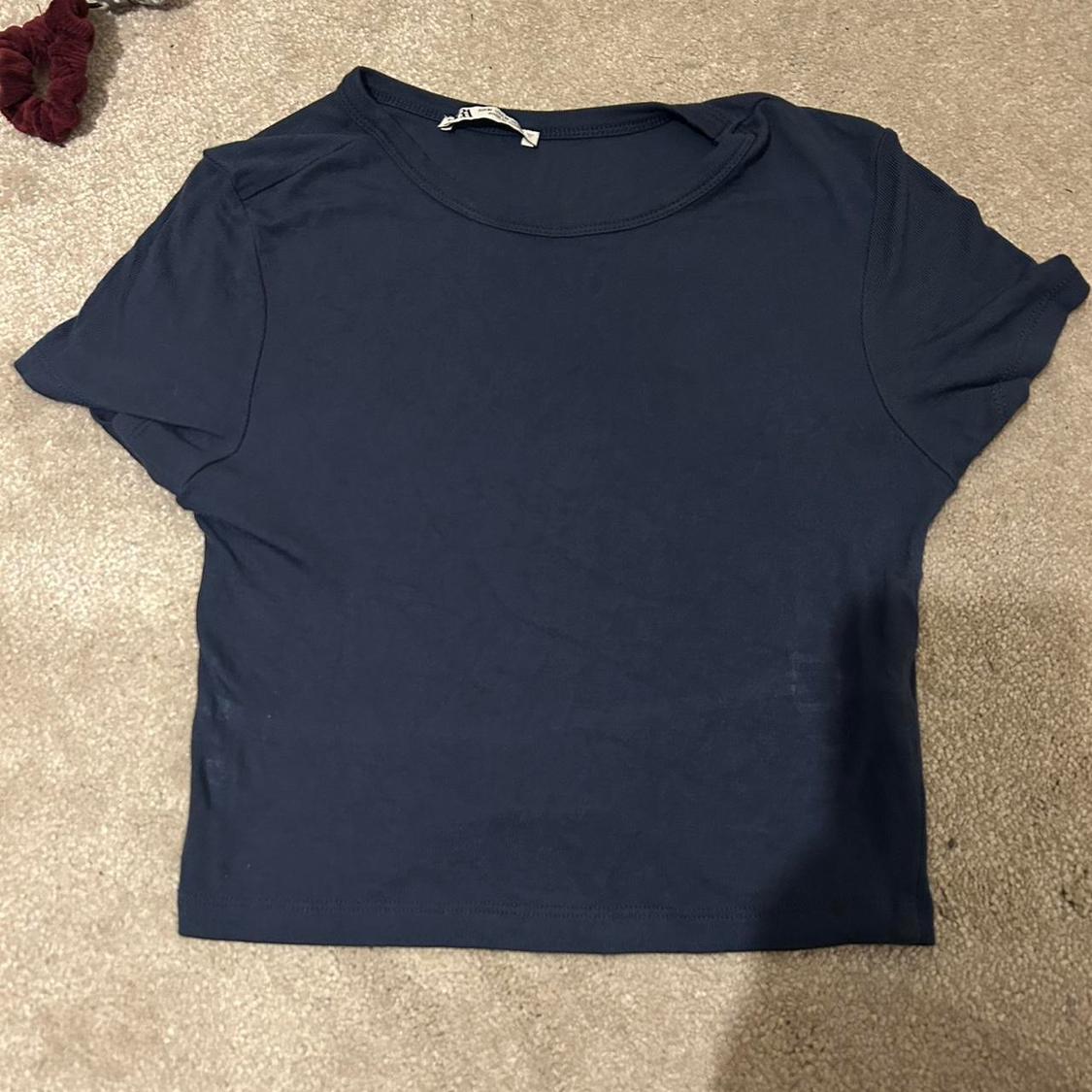 Navy blue short-sleeved T-shirt on a beige carpet, with a visible label on the collar.