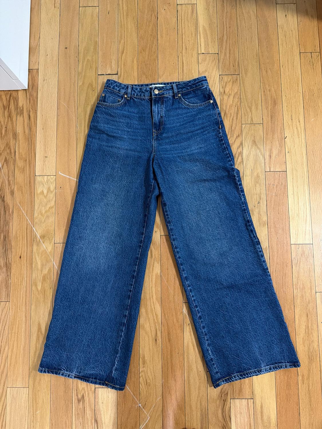 Blue wide-leg high-rise jeans, laid flat on a wooden floor. Casual style.