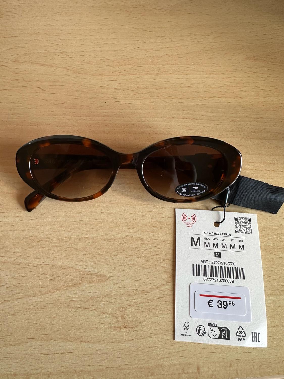Oval tortoiseshell sunglasses on wood. Text: ZARA Category 3 SIZE / SIZE / SIZE M ART.: 2727/210/700 €39.95