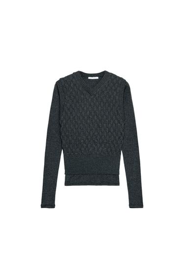 Front view of a grey T-shirt with a V-neckline and long sleeves. Detail of a knitted waistcoat overlay on the chest.