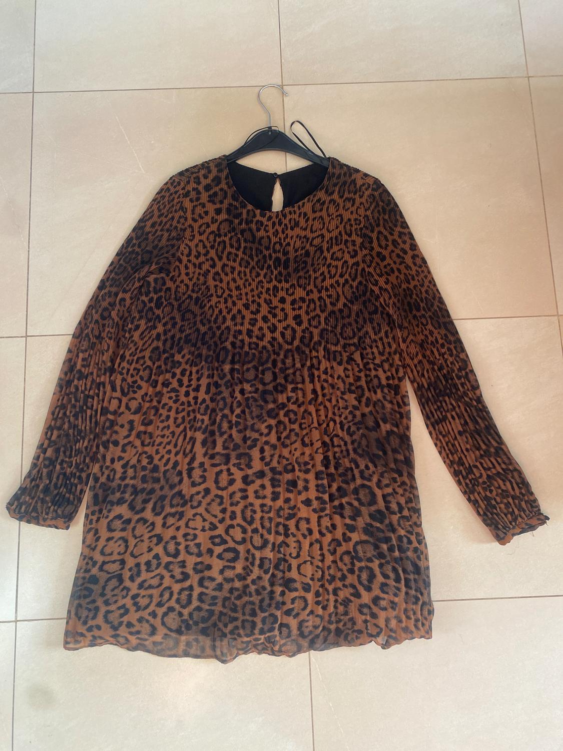 Long-sleeved leopard print dress in brown and black tones, hanging on a hanger over a light-coloured floor.