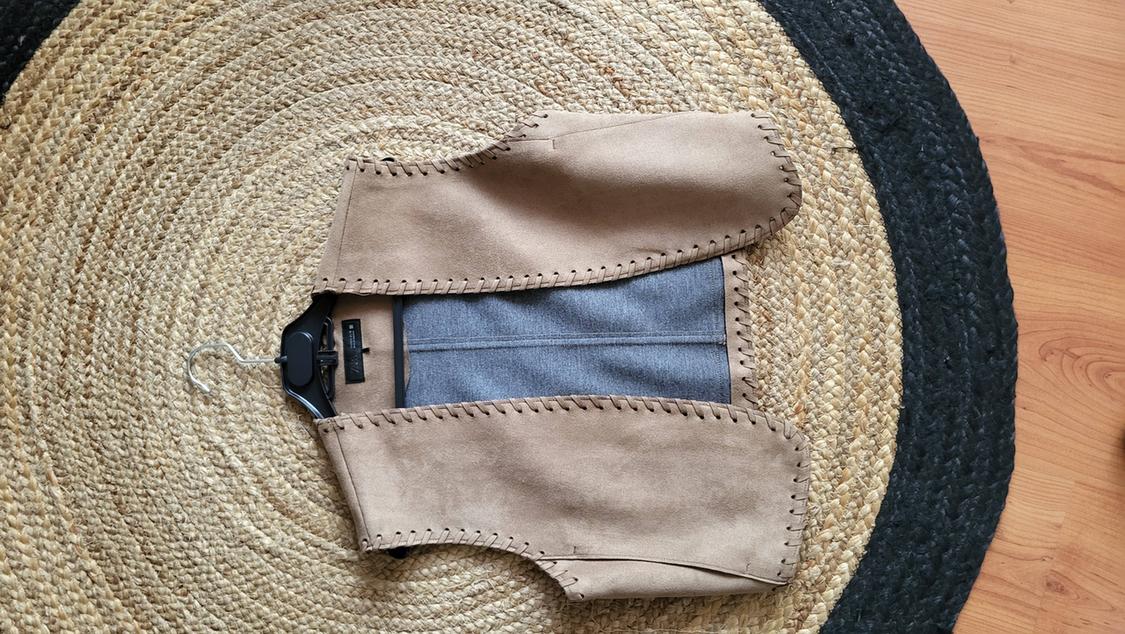 Beige waistcoat with visible stitching on a round jute rug. Light wood background.