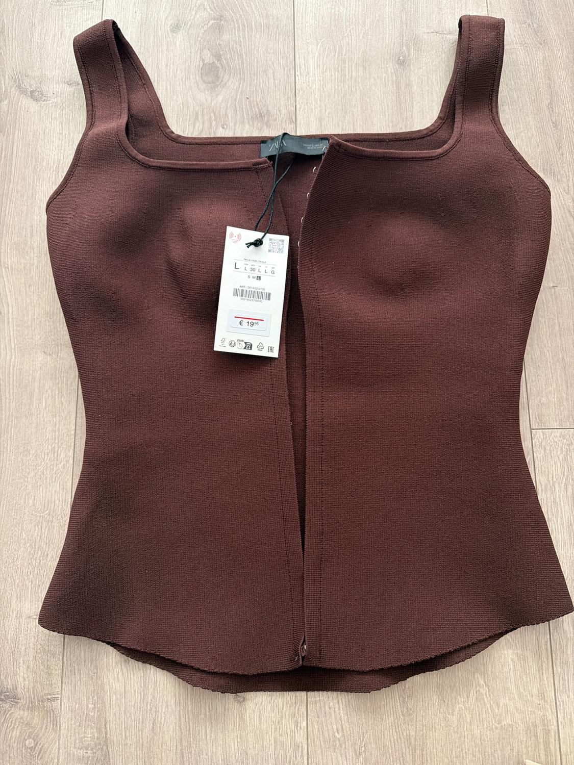 Brown sleeveless top on wooden floor, with visible price tag of 19€. Fitted design with square neckline.