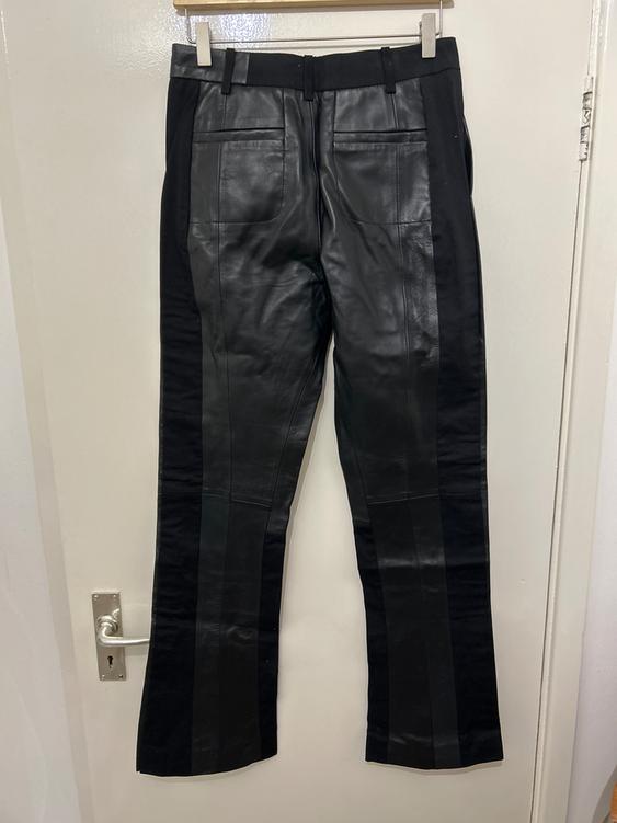 Black leather trousers hanging on a white door, with back pockets and belt loops.
