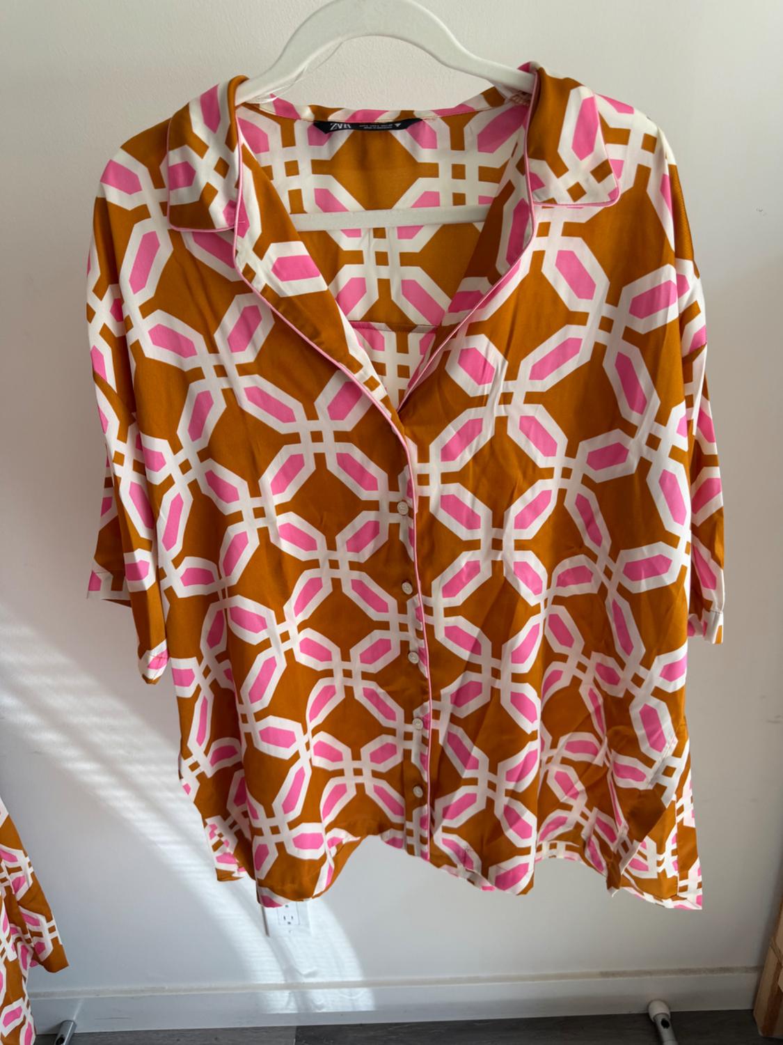 Shirt, hanging, with a geometric pattern in shades of brown, pink, and white. White background and grey wooden floor.