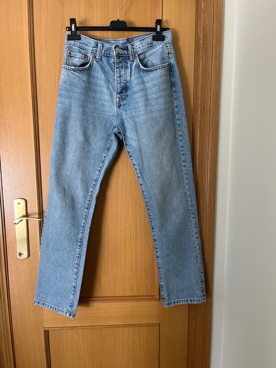 Blue jeans hanging on a black hanger over a light wooden door. Classic five-pocket design with button fastening.