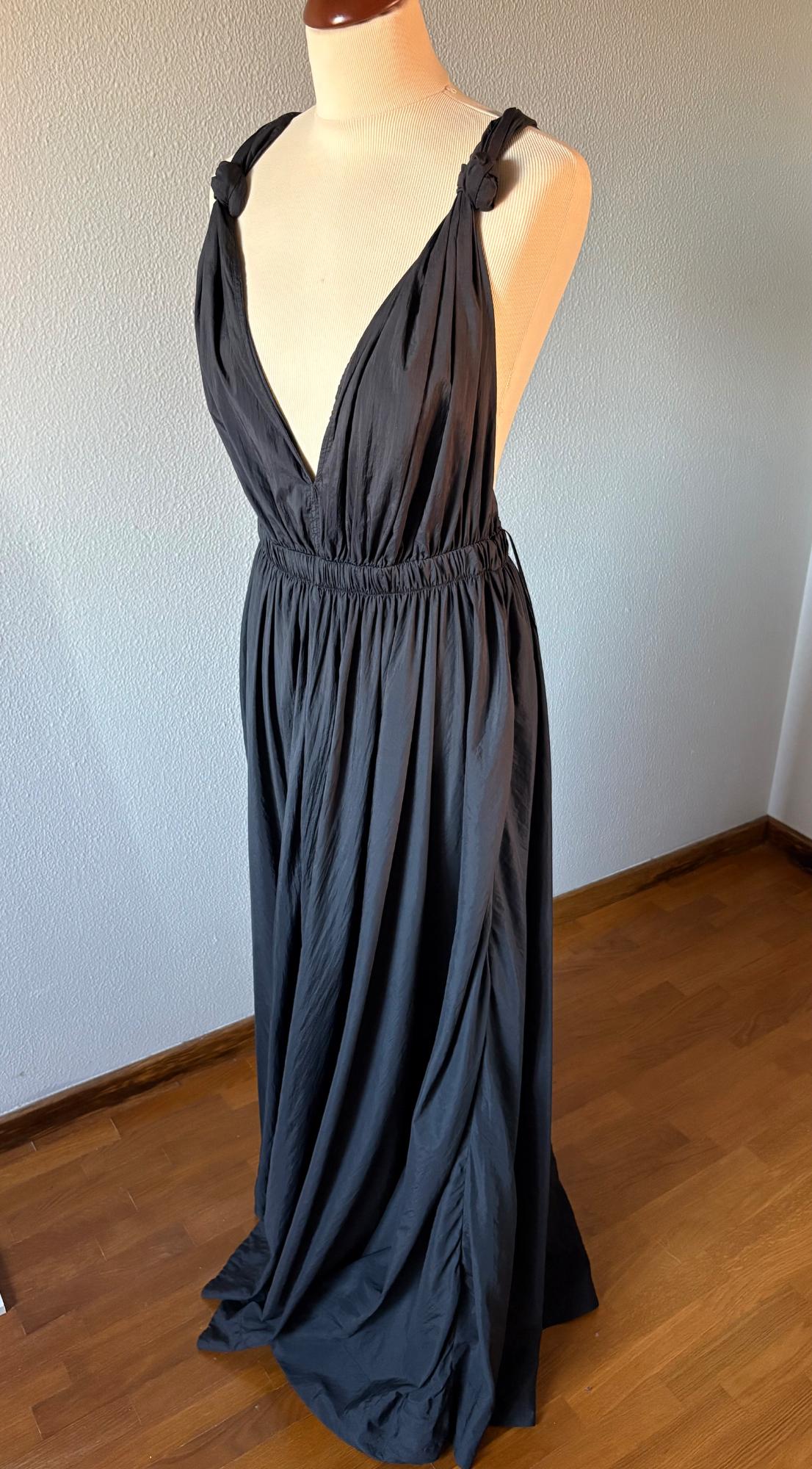 Mannequin in a long black dress with wide straps and a deep neckline, on a wooden floor with a white wall in the background.
