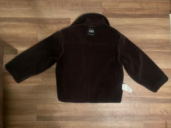 Black wool jacket seen from behind on a wooden floor. Visible label with the text "ZARA".