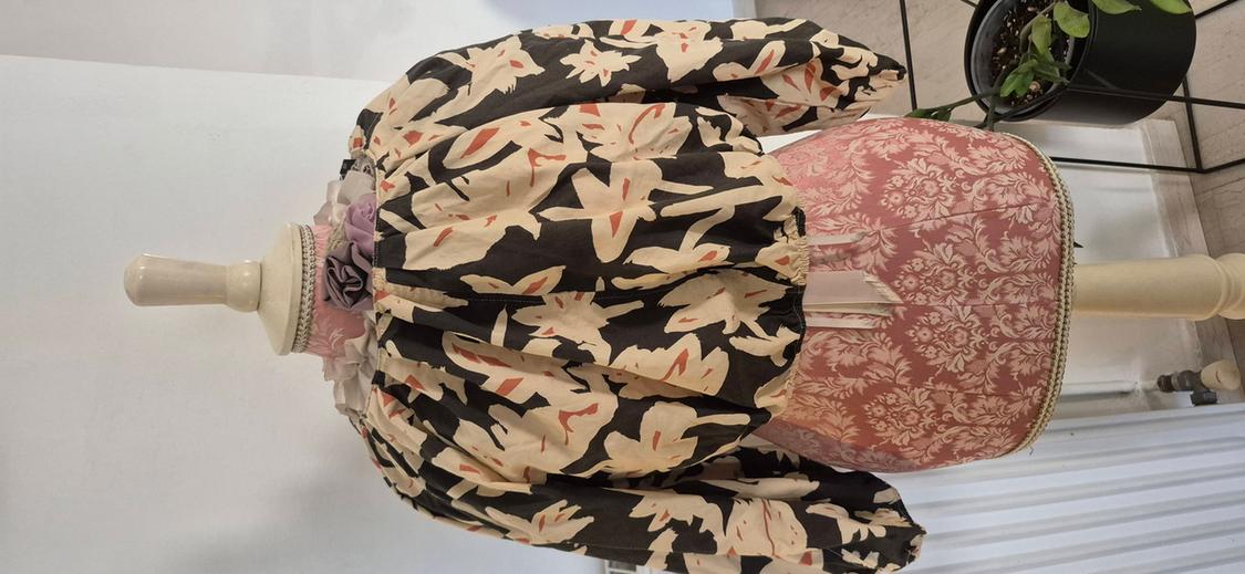 Mannequin in a long-sleeved blouse with a beige and black print, on a white background. Mannequin base with a pink floral design.
