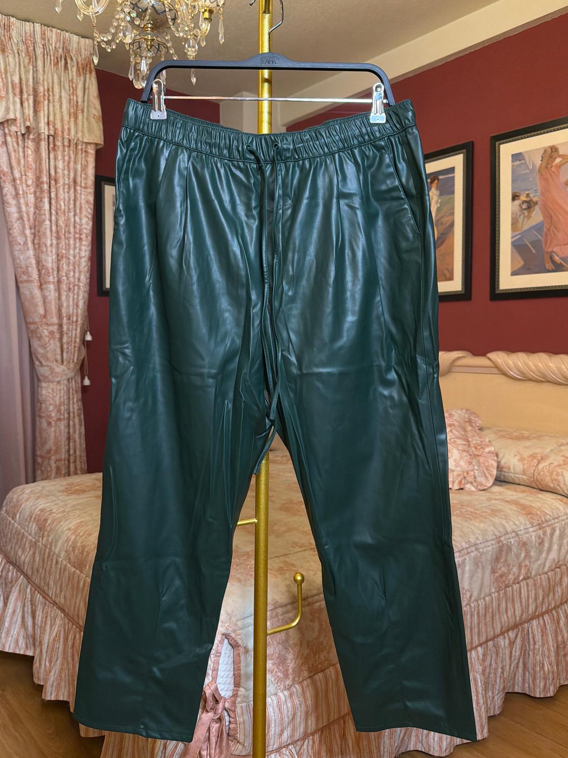 Green trousers hung on a gold hanger in a bedroom with pink-toned curtains and bed. Classic and elegant decor.