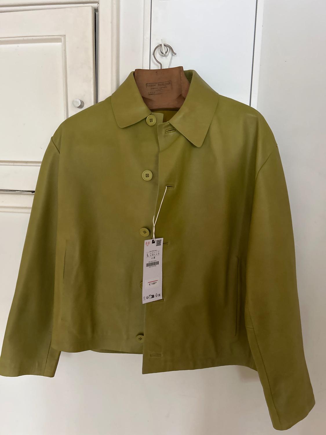 Olive green jacket hanging on a wooden hanger, with visible tag. White background with wardrobe door.