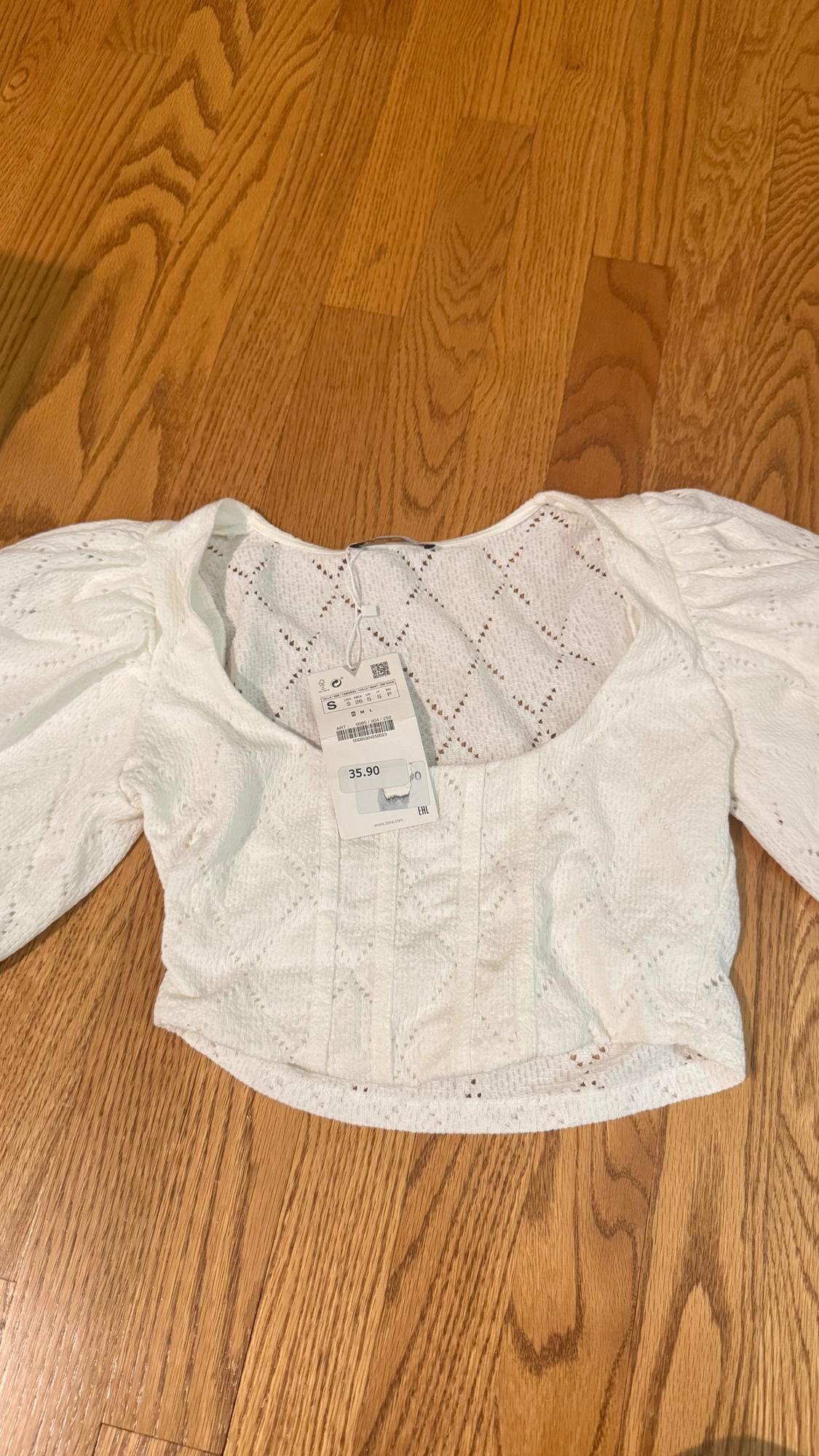 White lace blouse with puff sleeves on a wooden floor. Visible tag with a price of 35.90.
