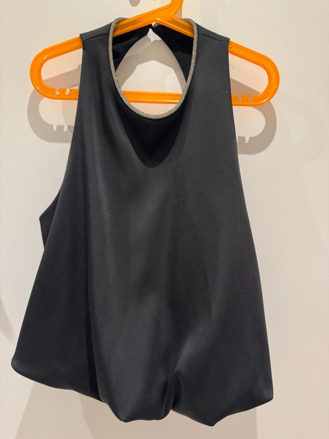 Black top with halter neck and a shiny detail, hung on an orange hanger on a white wall.