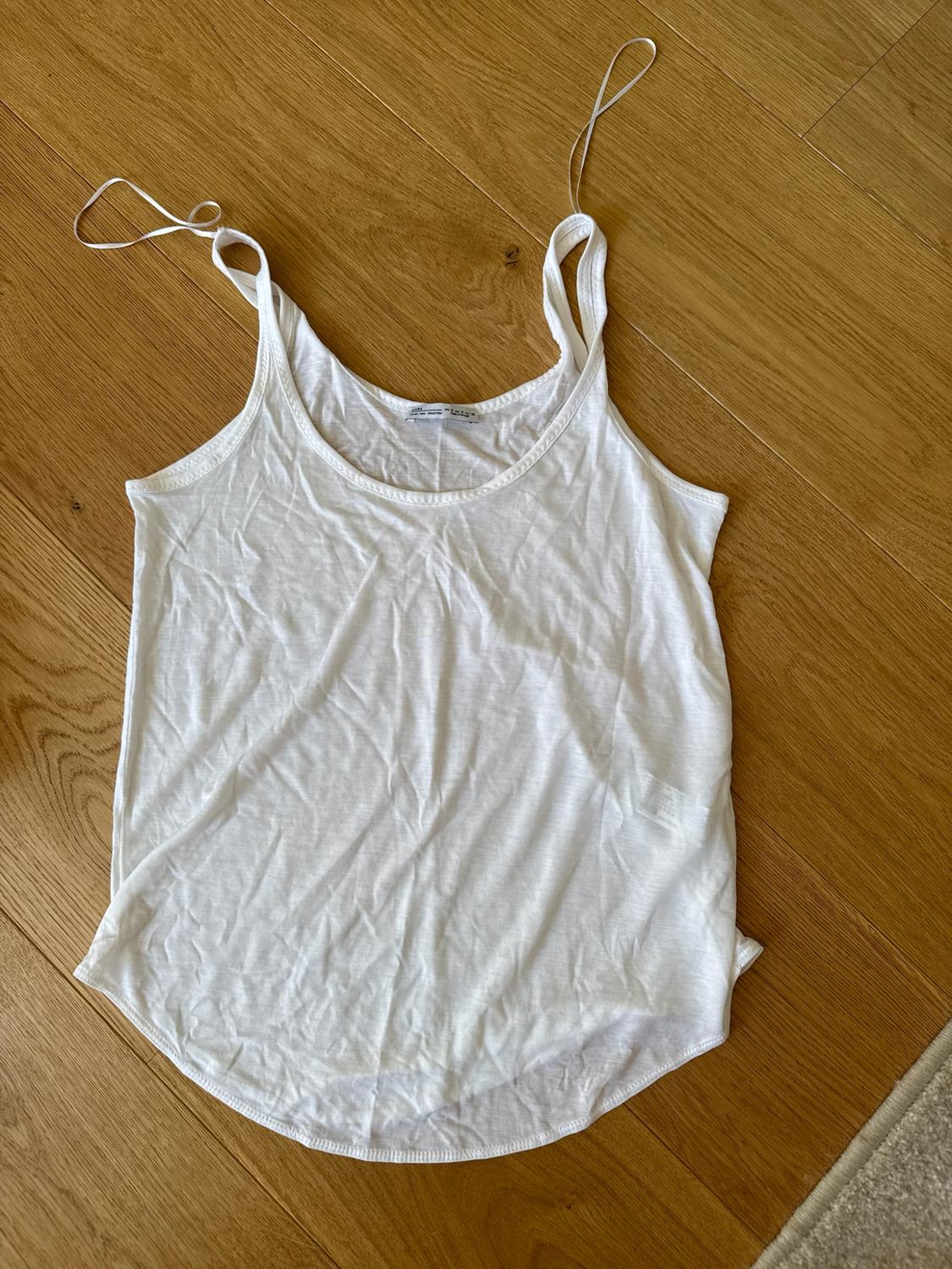 Basic white camisole top on a light wooden floor.