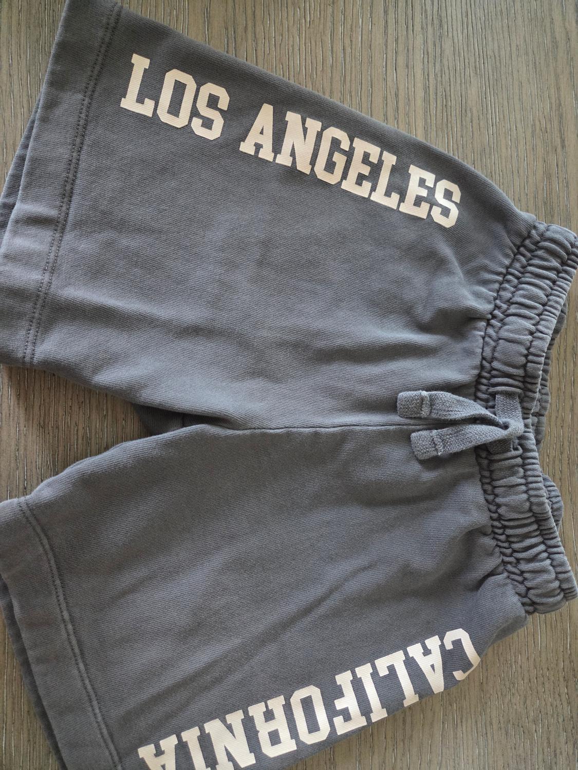Grey shorts with "LOS ANGELES" and "CALIFORNIA" text in white letters, on a wooden surface.