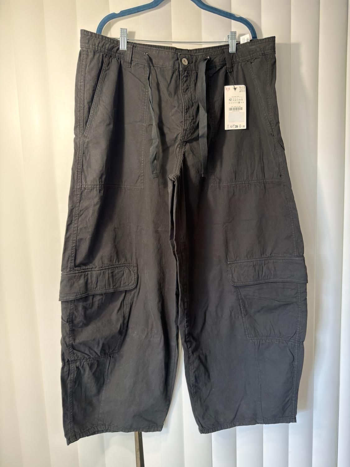 Dark gray cargo pants hanging on a blue hanger, with large side pockets and a price tag showing the number 42.