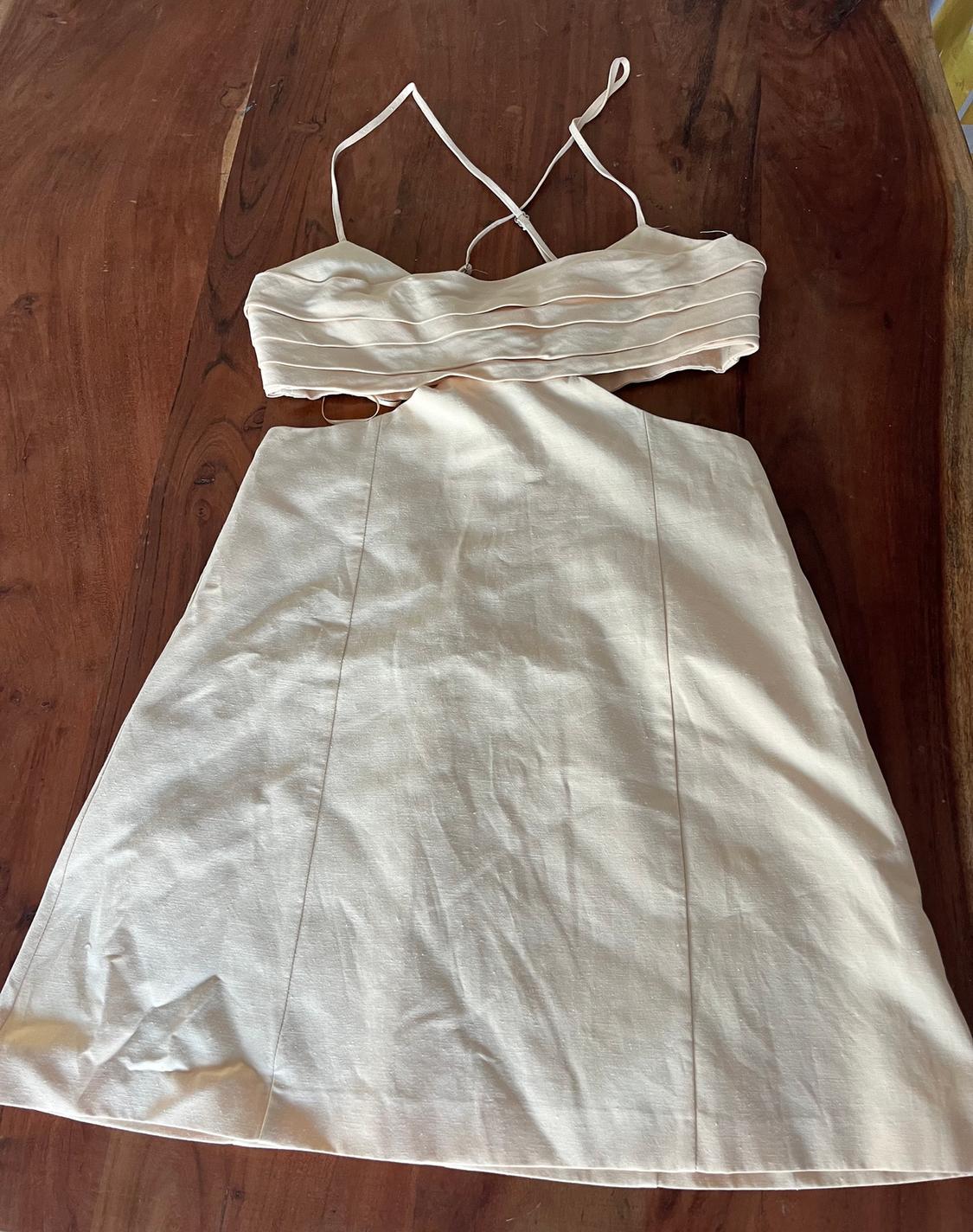 Beige sleeveless dress with thin cross-back straps, on a wooden table.