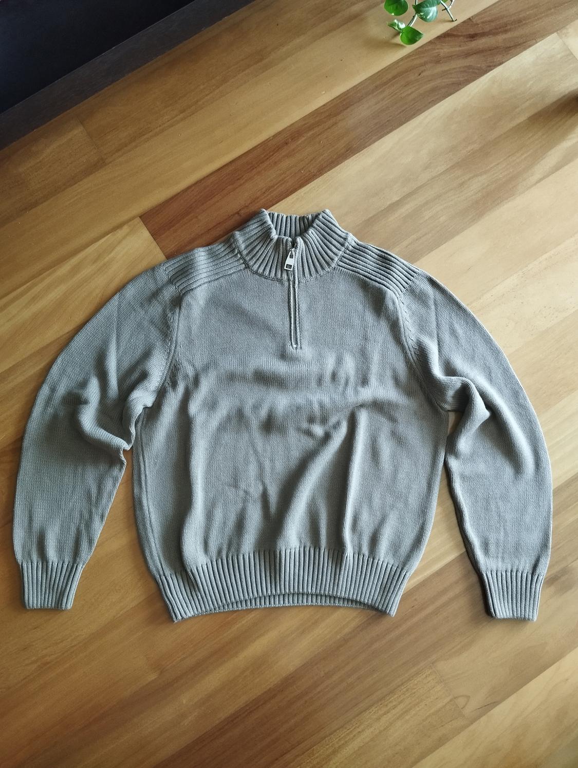 Grey knitted jumper with a zip-up neck, placed on a light wooden table.