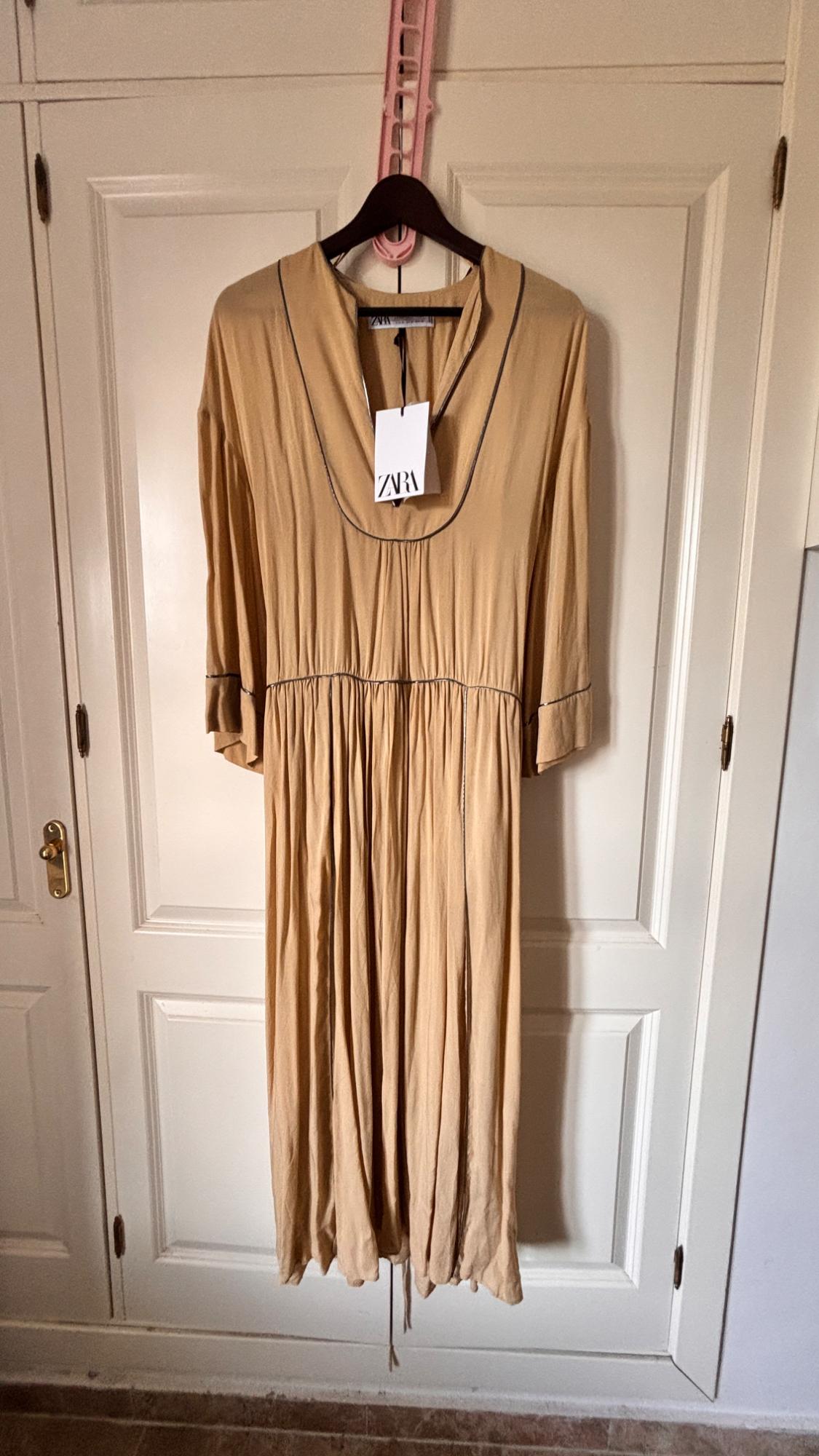 Beige three-quarter sleeve dress hanging on a black hanger with a Zara tag, over a white door.