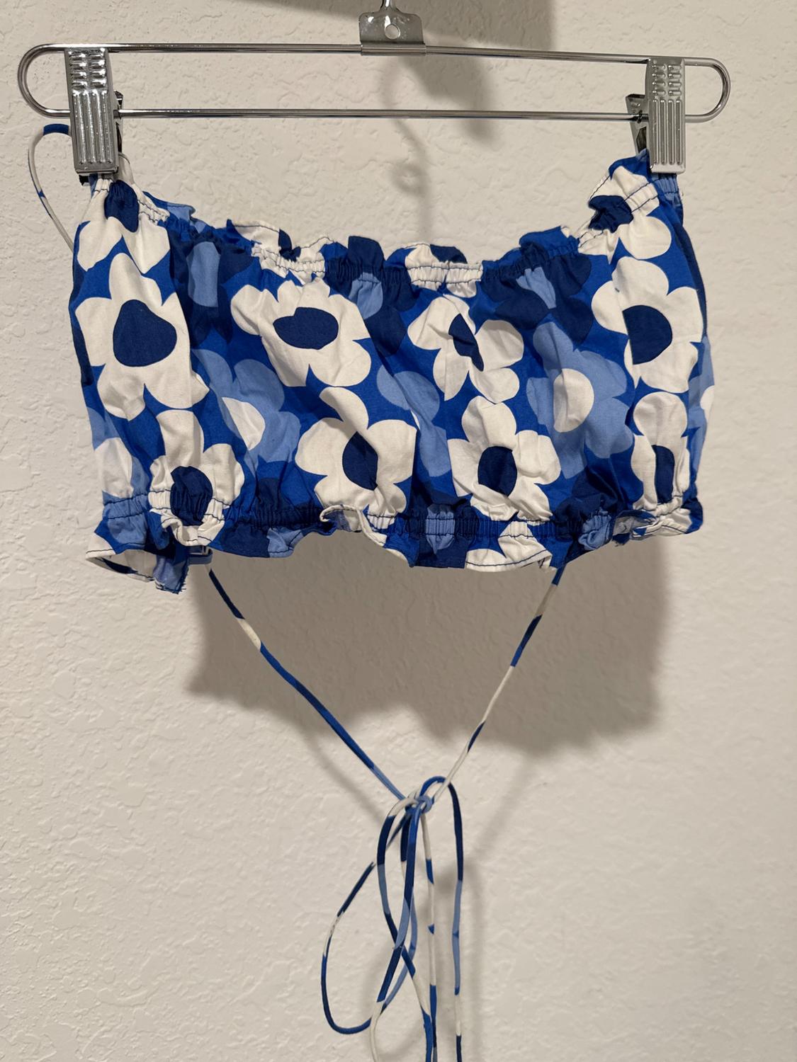 Crop top with blue and white floral print, hanging on a metal hanger against a white wall.