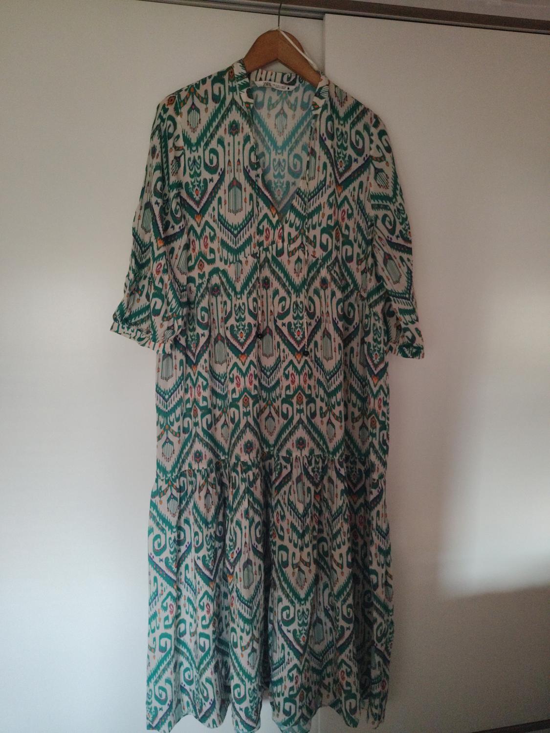 Dress hanging on a hanger with a geometric print in green and white tones, against a white wardrobe background.