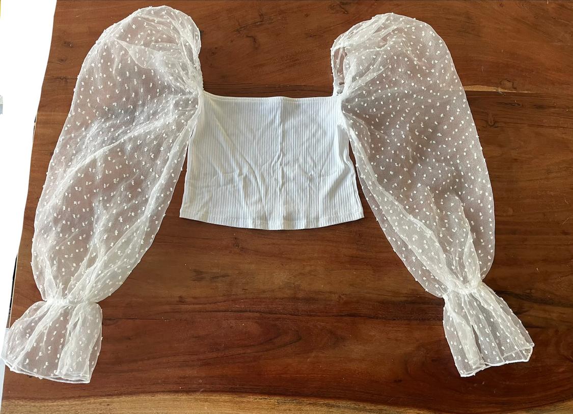 White top with sheer spot-tulle long sleeves, on a wooden table.