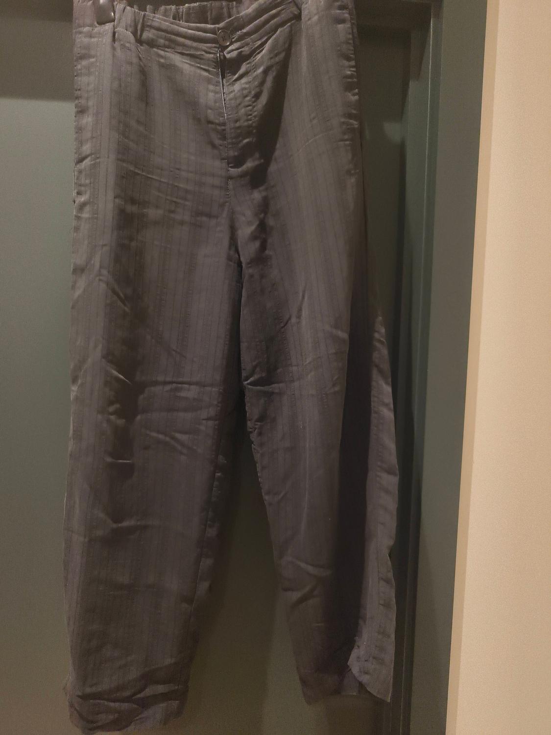 Textured grey trousers hung on a hanger over a green door. The fabric has a subtle striped pattern.